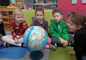 Grupka dzieci siedzi na podłodze i ogląda globus.