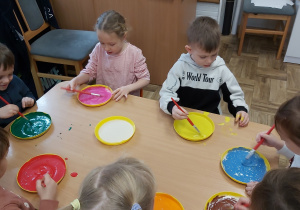Dzieci siedząc przy stoliku i mieszają różne kolory farb na przygotowanych miseczkach. Poznają przy tym nową technikę plastyczną - tworzenie farb puchnących.