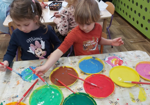 Dziewczynka i chłopiec malują farbami- tworzą planety.