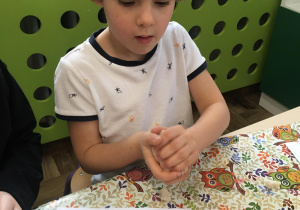 Chłopiec w iałej bluzce wycina z masy solnej gwiazdki za pomocą foremki.