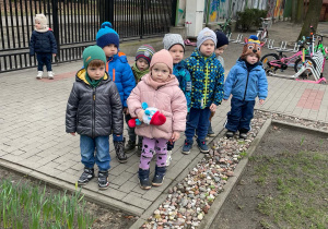 Grupa dzieci stoi w przedszkolnym ogrodzie aby szukać oznak wiosny,