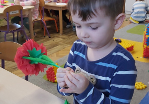 Chłopiec wykonuje kwiatek z czerwonej krepiny.