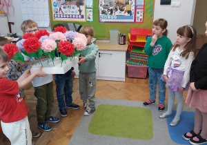 Grupa chłopców stoi z bukietem kwiatów przed dziewczynkami.