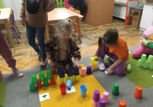 Dwie dziewczynki układają wieżę z kolorowych kubków wg ustalonego kodu.