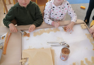 Dziewczynka i chłopiec smarują masą kajmakową wycięte waflowe ciasteczka.