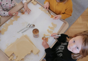 Dwie dziewczynkai smarują masą kajmakową wycięte waflowe ciasteczka.