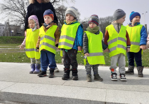 Dzieci ubrane w odblaskowe kamizelki pozują do zdjęcia stojąc na Bulwarach Wiślanych.