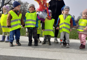 Dzieci ubrane w odblaskowe kamizelki pozują do zdjęcia stojąc z Marzanną na Bulwarach Wiślanych.