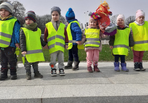 Dzieci ubrane w odblaskowe kamizelki pozują do zdjęcia stojąc z Marzanną na Bulwarach Wiślanych.