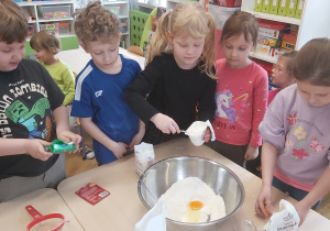 Grupka dzieci przekłada do metalowej miski składniki potrzebne do wykonania ciasta.