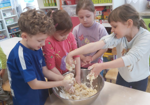 Czworo dzieci wyrabia rękami ciasto w metalowej misce.