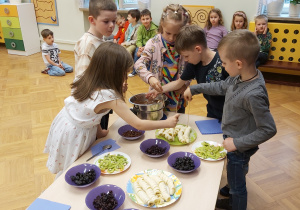 Dzieci nadziewają przygotowane owoce i bakalie na patyczki do szaszłyków.
