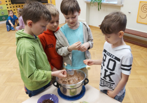 Chłopcy zanurzają owocowe szaszłyki w roztopionej czekoladzie.