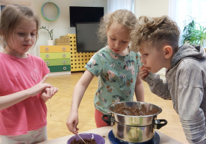 Troje dzieci zajada umoczone w czekoladzie owocowe szaszłyki.