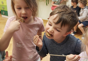 Dziewczynka i chłopiec jedzą banany umoczone w czekoladzie.