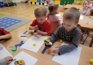 Dzieci wyklejają na kartce z figur geometrycznych pajacyka