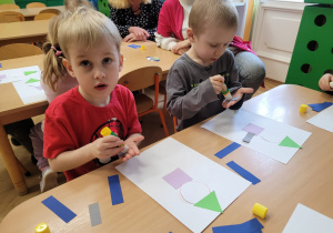 Dzieci wyklejają na kartce z figur geometrycznych pajacyka
