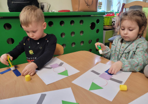 Dzieci wyklejają na kartce z figur geometrycznych pajacyka