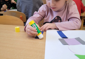 Dziecko wykleja na kartce z figur geometrycznych pajacyka