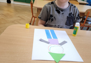 Dziecko wykleja na kartce z figur geometrycznych pajacyka