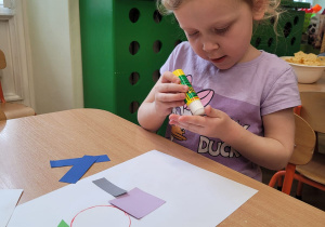 Dziecko wykleja na kartce z figur geometrycznych pajacyka
