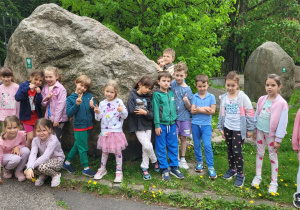 Grupa dzieci pozuje do zdjęcia na tle ogromnego głazu- Pomnika Przyrody.