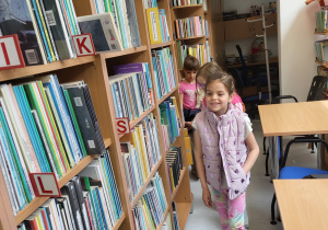 Dzieci spacerują pomiędzy bibliotecznymi półkami.
