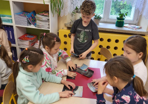 Grupa dzieci układa obraz z kawałków- puzzli.