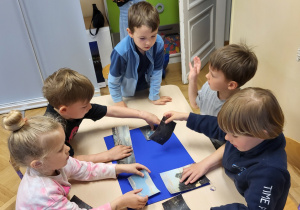 Grupa dzieci układa obraz z kawałków- puzzli.