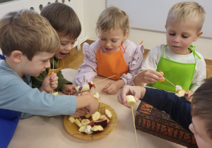 Dzieci nadziewają na patyczki kawałki owoców.