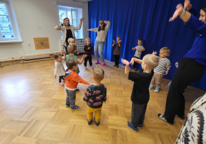 Dzieci z maluszków stoją w kółku i machają rękami .