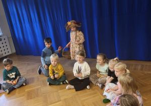 Dzieci z grupy 5 i 6 latków siedzą w kole i śpiewają piosenkę o darach Pani Jesieni. Jedna z dziewczynek w stroju Pani Jesieni chodzi dookoła dzieci i rozdaje im jesienne dary.