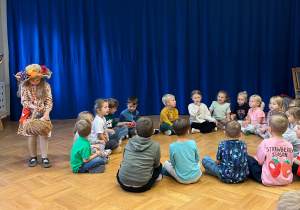 Dzieci z grupy 5 i 6 latków siedzą w kole i śpiewają piosenkę o darach Pani Jesieni. Jedna z dziewczynek w stroju Pani Jesieni chodzi dookoła dzieci i rozdaje im jesienne dary.