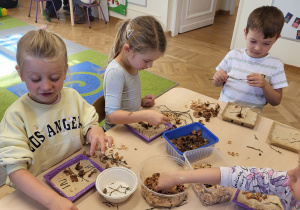 Dzieci układają obrazki z materiału przyrodniczego. Układają je na pudełku z gipsem.