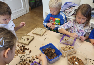 Dzieci układają obrazki z materiału przyrodniczego. Układają je na pudełku z gipsem.