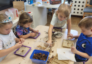 Dzieci układają obrazki z materiału przyrodniczego wg własnego pomysłu. Wykorzystują patyczki, pestki dyni oraz łupinki z pistacji.
