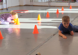 Dzieci wykonują na podłodze zadane im ćwiczenia gimnastyczne.
