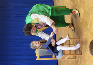 Dziewczynka siedzi na krześle i robi z klaunem sztuczkę z czerwonymi piłeczkami.