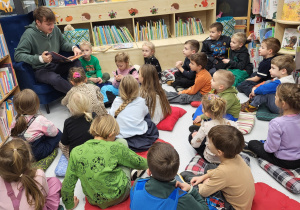 Dzieci siedzą na dywanie i słuchają czytanej książki.