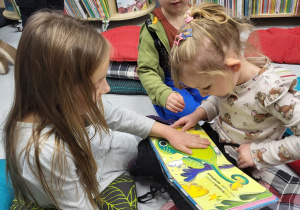 Dwie dziewczynki oglądają książkę z pokazanymi różnymi fakturami materiału.