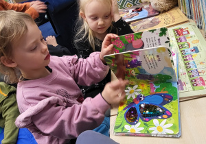 Dzieci oglądają książkę sensoryczną, z pokazanymi różnymi fakturami materiału.