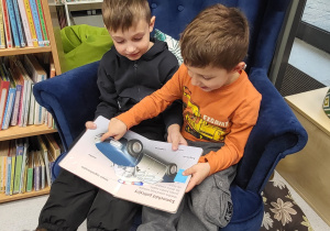 Dwaj chłopcy oglądają książkę z modelami różnych samochodów.