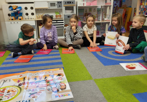 Dzieci siedzą na dywanie i dopasowują ilustracje z art. spożywczymi do piramidy zdrowego żywienia.