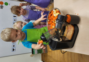 Chłopiec wrzuca kawałki marchewki do sokowirówki.