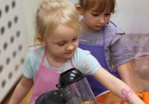 Dziewczynka wrzuca kawałki jabłka do sokowirówki.