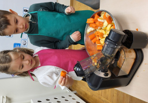 Dziewczynka i chłopiec wykonują sok z marchewki, jabłka i pomarańczy za pomocą sokowirówki sokowirówki.