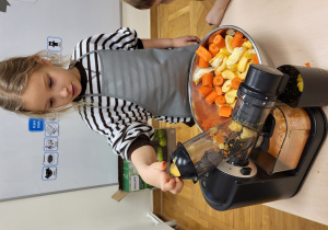 Dziewczynka wrzuca kawałki jabłka do sokowirówki.