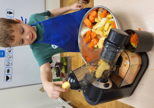 Chłopiec wrzuca kawałki jabłka do sokowirówki.