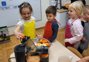 Dzieci wykonują sok z marchewki, jabłka i pomarańczy za pomocą sokowirówki sokowirówki.