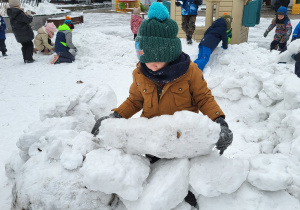 Chłopiec buduje igloo z brył śniegu.